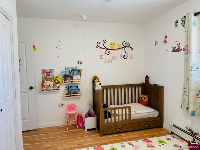 bedroom featuring a baseboard heating unit, wood finished floors, and baseboards