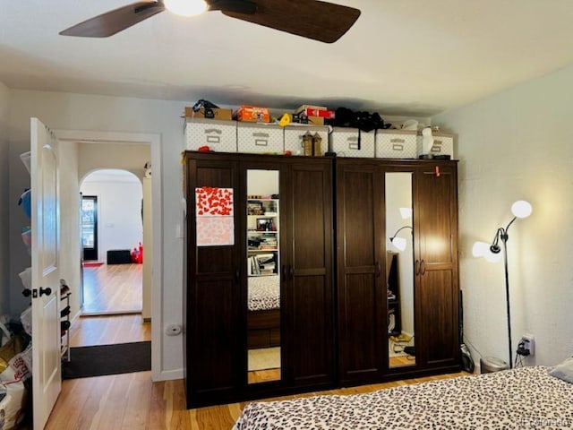 bedroom with light wood-type flooring, arched walkways, and a ceiling fan