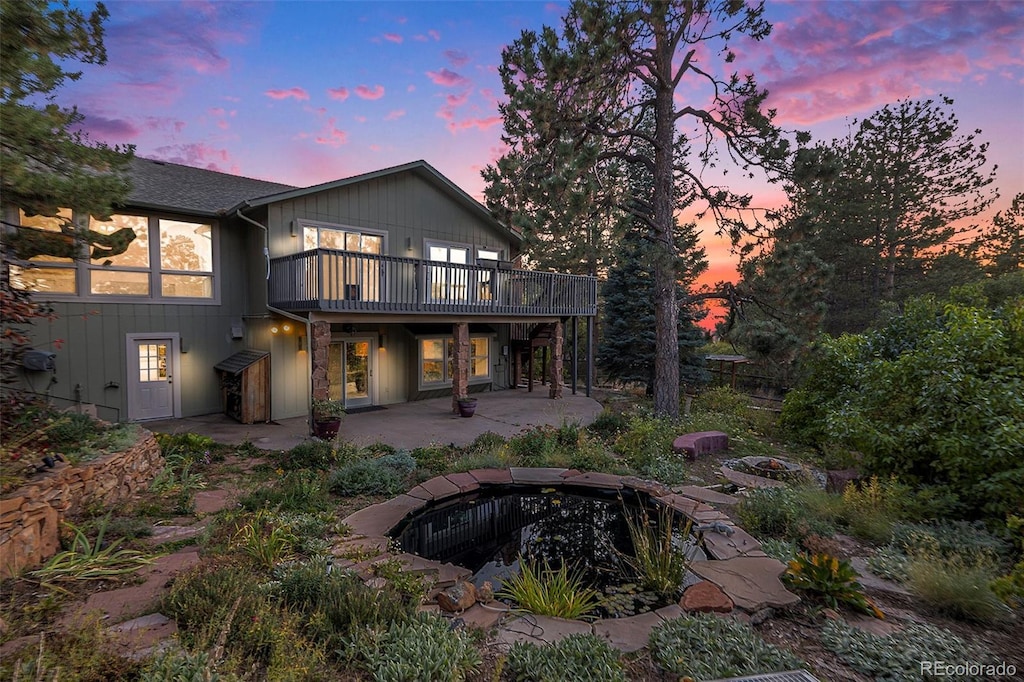 back house at dusk with a wooden deck, a patio area, and a fire pit