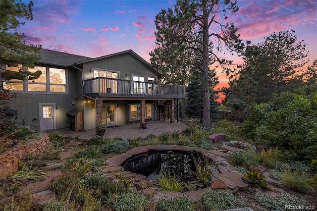 back house at dusk with a wooden deck, a patio area, and a fire pit