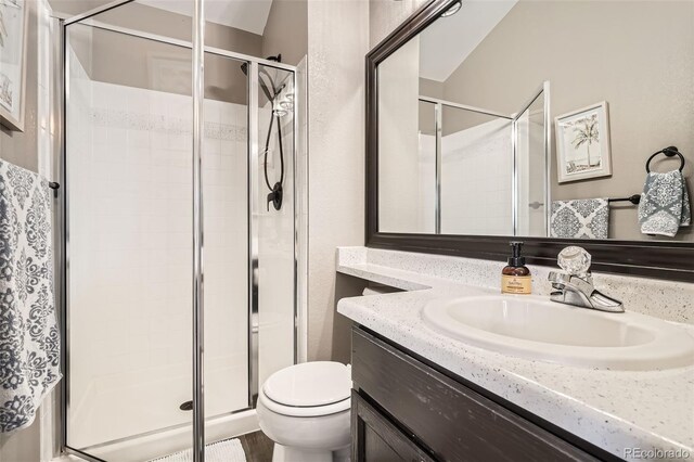 bathroom with vanity, toilet, a textured wall, and a stall shower