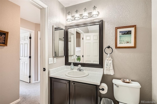 bathroom featuring vanity, toilet, a textured wall, and baseboards