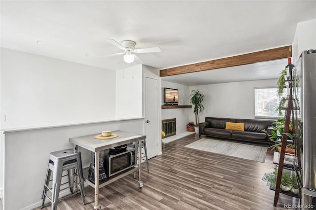 living room featuring a brick fireplace, hardwood / wood-style floors, beamed ceiling, and ceiling fan