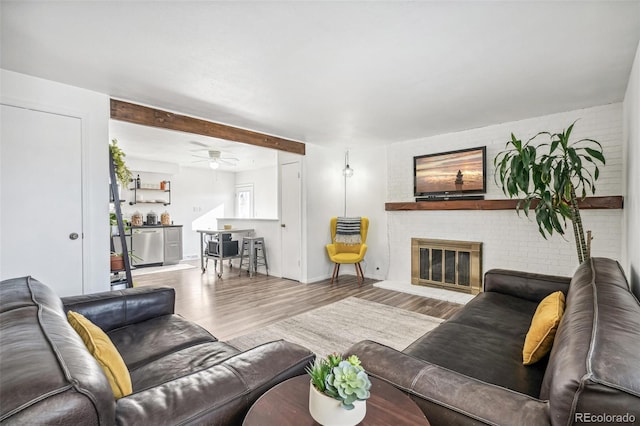 living area with brick wall, a brick fireplace, wood finished floors, and baseboards