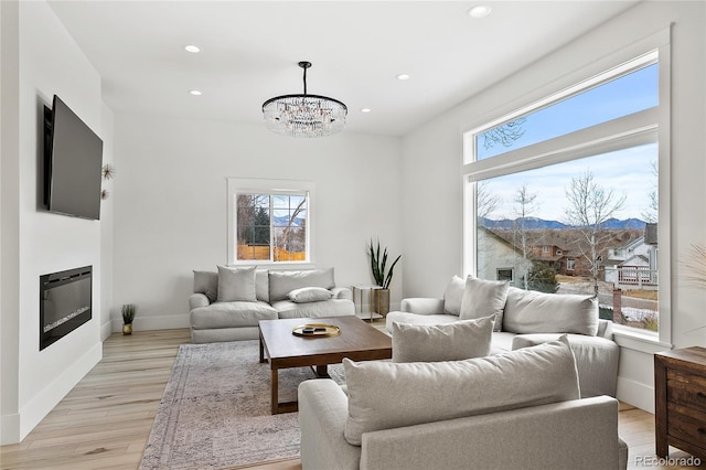 living room with light wood-type flooring, a glass covered fireplace, a wealth of natural light, and recessed lighting