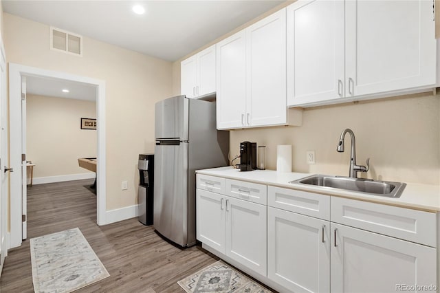 kitchen featuring a sink, visible vents, white cabinetry, freestanding refrigerator, and light wood finished floors