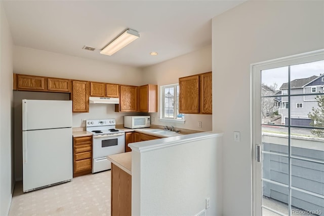 kitchen with white appliances, under cabinet range hood, brown cabinetry, and light countertops