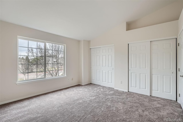 unfurnished bedroom with two closets, carpet floors, lofted ceiling, and baseboards