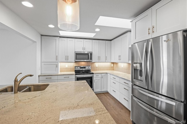 kitchen with light stone countertops, sink, backsplash, white cabinets, and appliances with stainless steel finishes