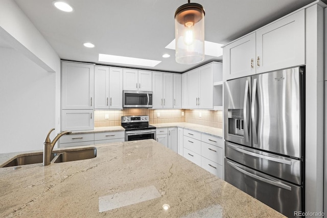 kitchen with light stone countertops, sink, stainless steel appliances, pendant lighting, and white cabinets