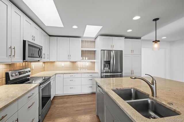 kitchen with appliances with stainless steel finishes, a skylight, sink, pendant lighting, and white cabinetry