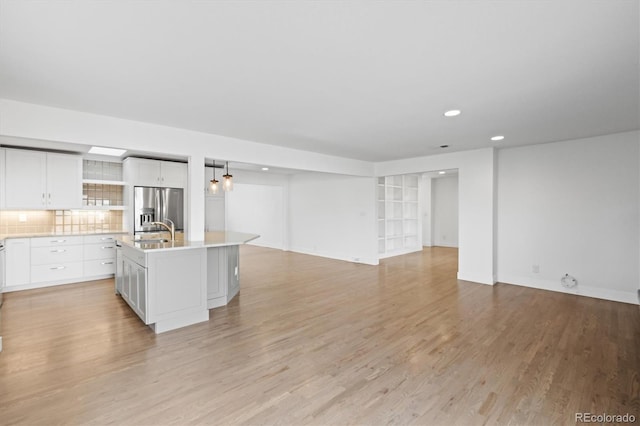 kitchen with decorative backsplash, stainless steel fridge, a kitchen island with sink, sink, and white cabinetry