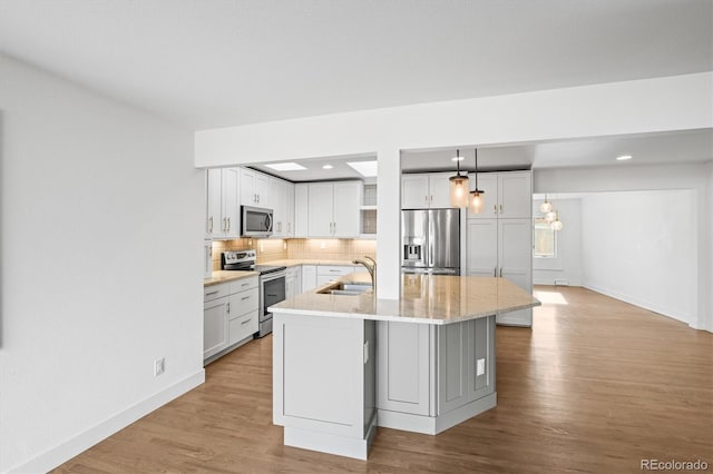 kitchen with sink, hanging light fixtures, stainless steel appliances, a center island with sink, and white cabinets