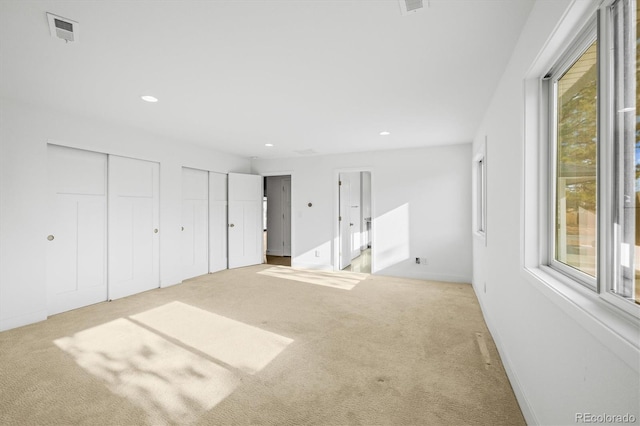 unfurnished bedroom featuring light colored carpet and multiple closets