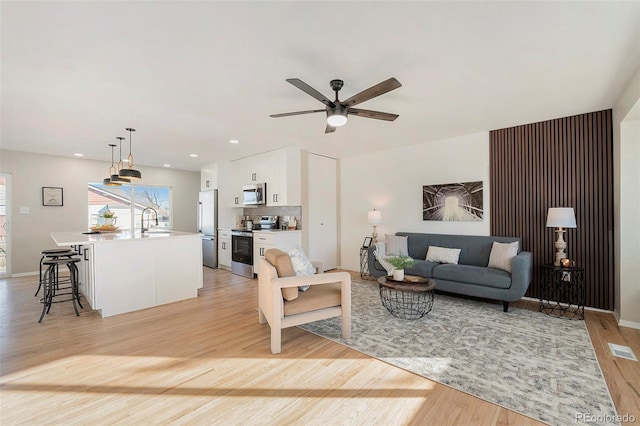 living room featuring ceiling fan, sink, and light hardwood / wood-style flooring