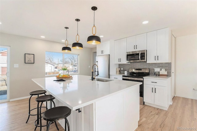 kitchen with pendant lighting, white cabinetry, stainless steel appliances, and a center island with sink