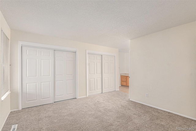 unfurnished bedroom with light colored carpet, a textured ceiling, and multiple closets