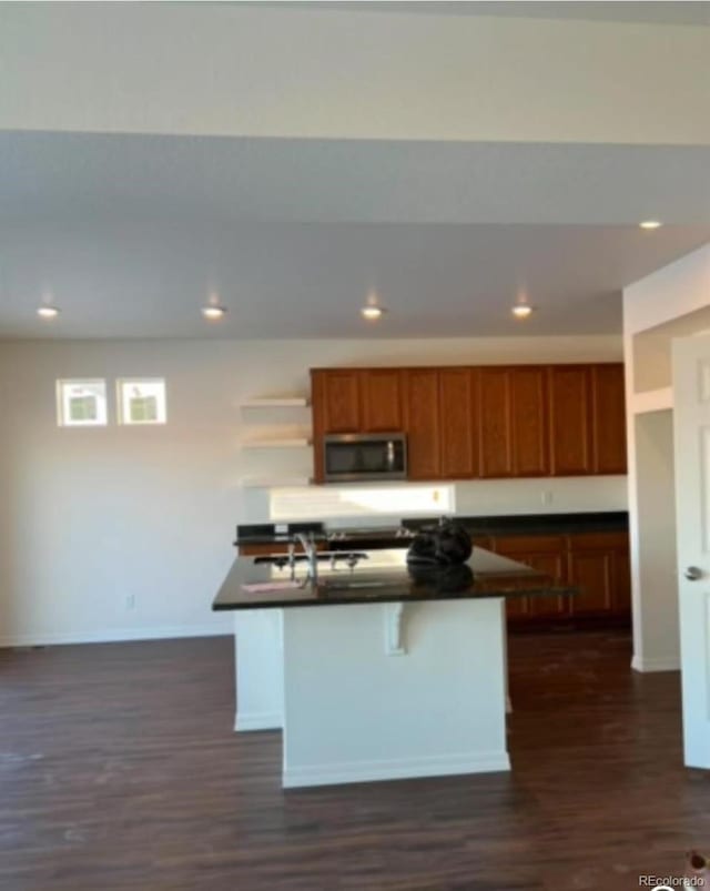 kitchen with sink, dark hardwood / wood-style flooring, a kitchen bar, and an island with sink