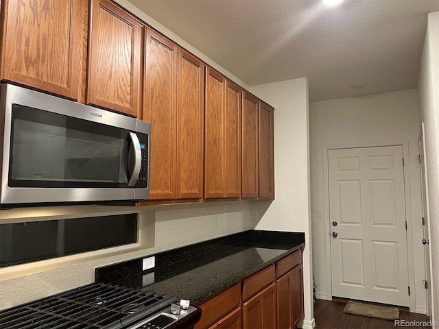 kitchen with stainless steel appliances, dark stone counters, and dark hardwood / wood-style floors