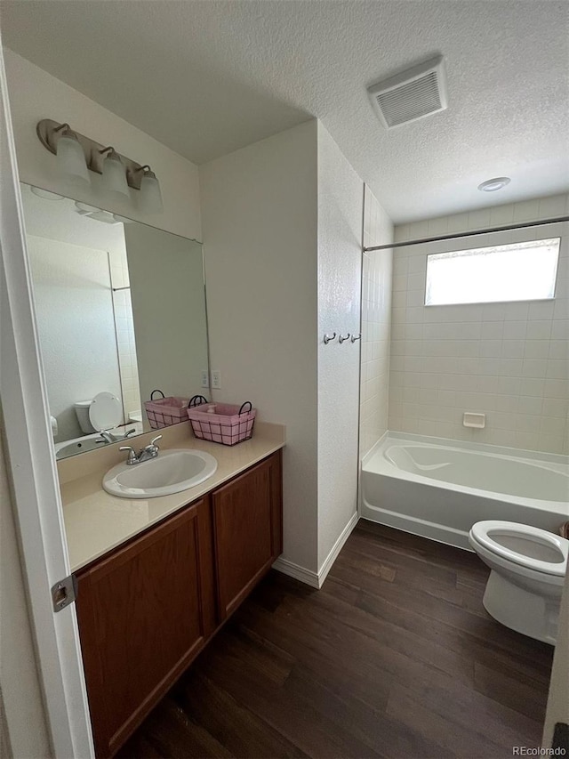 full bathroom with toilet, hardwood / wood-style flooring, a textured ceiling, tiled shower / bath, and vanity