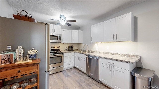 13626 E Bates Ave Unit 302, Aurora, CO 80014 - kitchen with stainless steel appliances, a ceiling fan, white cabinets, light wood-style floors, and light stone counters