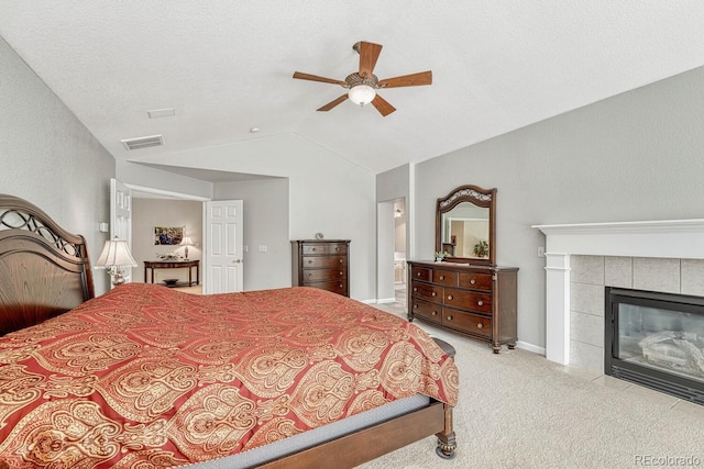 carpeted bedroom featuring ensuite bath, a textured ceiling, a tile fireplace, ceiling fan, and vaulted ceiling