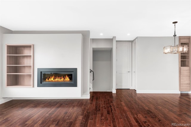 unfurnished living room featuring a notable chandelier, dark hardwood / wood-style flooring, and built in features