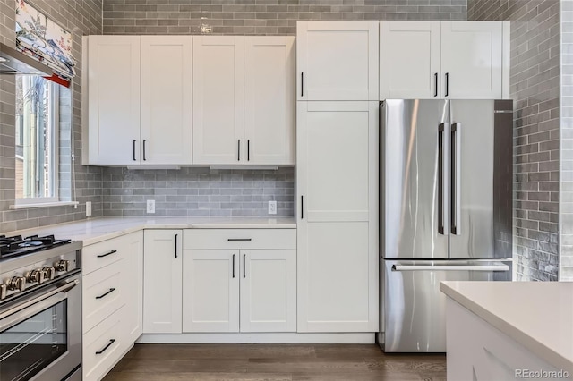 kitchen with wall chimney exhaust hood, backsplash, white cabinetry, dark wood-type flooring, and stainless steel appliances