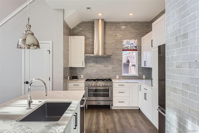 kitchen featuring appliances with stainless steel finishes, sink, backsplash, white cabinetry, and wall chimney range hood