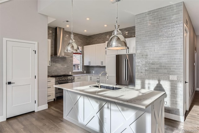 kitchen with wall chimney exhaust hood, white cabinetry, high end appliances, sink, and a kitchen island with sink