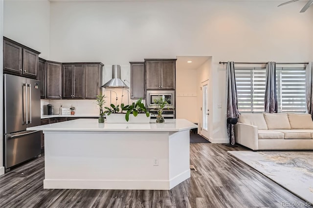 10095 E 59th Ave, Denver, CO 80238 - kitchen featuring appliances with stainless steel finishes, a high ceiling, wall chimney range hood, dark brown cabinetry, and light countertops