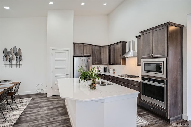 10095 E 59th Ave, Denver, CO 80238 - kitchen featuring stainless steel appliances, wall chimney exhaust hood, a high ceiling, dark brown cabinetry, and dark wood-style floors