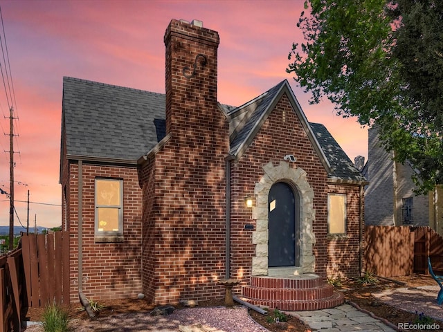 view of front of home featuring brick siding, fence, a shingled roof, and a chimney