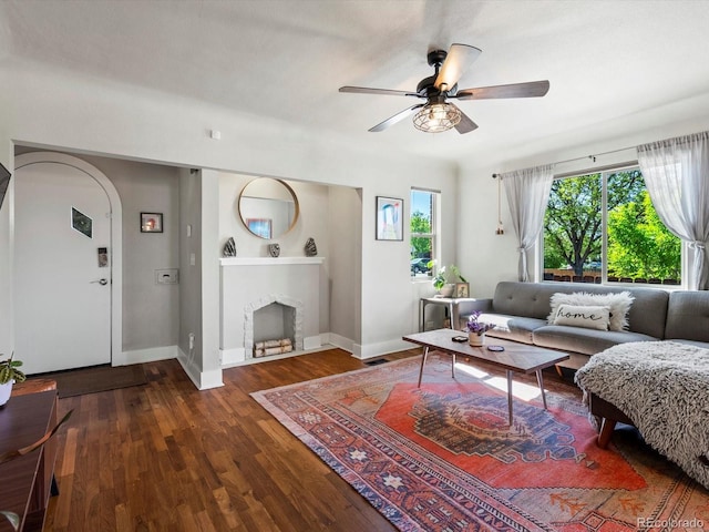 living room with a ceiling fan, baseboards, wood finished floors, a fireplace, and arched walkways