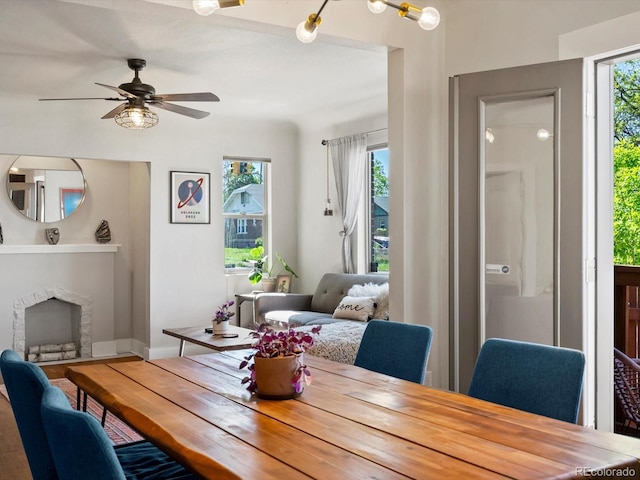dining space featuring a ceiling fan, a fireplace, wood finished floors, and baseboards