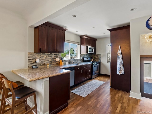 kitchen featuring appliances with stainless steel finishes, backsplash, a peninsula, a sink, and a kitchen bar
