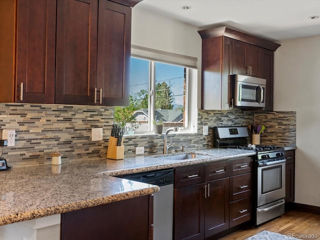 kitchen featuring appliances with stainless steel finishes, a sink, light wood-type flooring, light stone countertops, and decorative backsplash