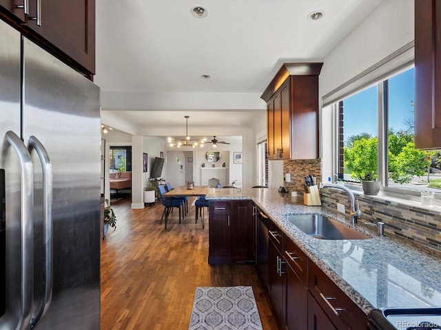 kitchen featuring stainless steel appliances, a sink, dark wood-type flooring, decorative backsplash, and light stone countertops