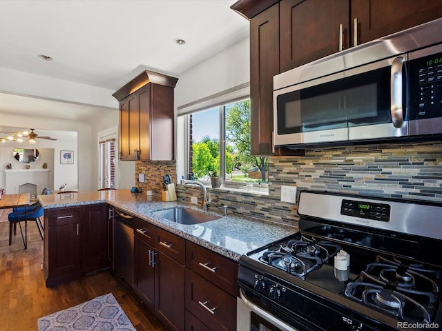 kitchen with appliances with stainless steel finishes, a sink, tasteful backsplash, dark wood-type flooring, and light stone countertops