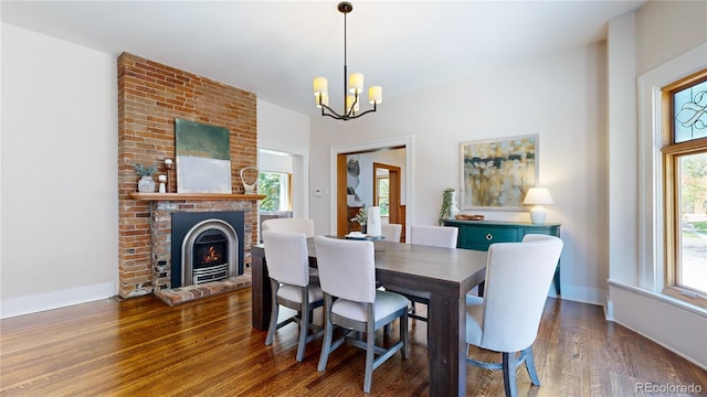 dining area with dark hardwood / wood-style flooring, brick wall, a brick fireplace, and an inviting chandelier