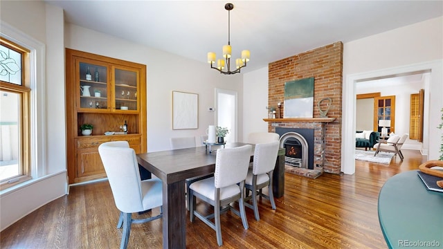 dining room featuring dark hardwood / wood-style floors, a notable chandelier, brick wall, and a brick fireplace