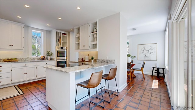 kitchen with light stone counters, white cabinets, dark tile flooring, stainless steel double oven, and a kitchen breakfast bar