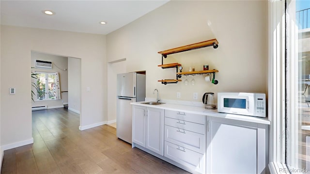 kitchen with white appliances, light wood-type flooring, white cabinetry, vaulted ceiling, and sink