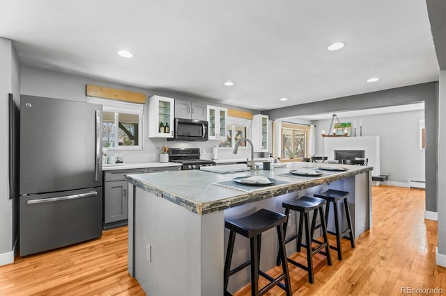 kitchen featuring a kitchen bar, baseboard heating, light wood-style flooring, and appliances with stainless steel finishes