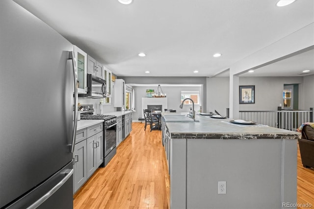 kitchen featuring a sink, open floor plan, appliances with stainless steel finishes, light wood finished floors, and glass insert cabinets