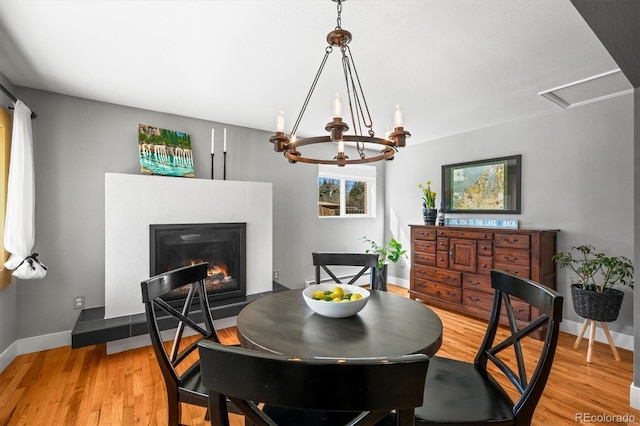 dining room featuring baseboards, a glass covered fireplace, and light wood finished floors