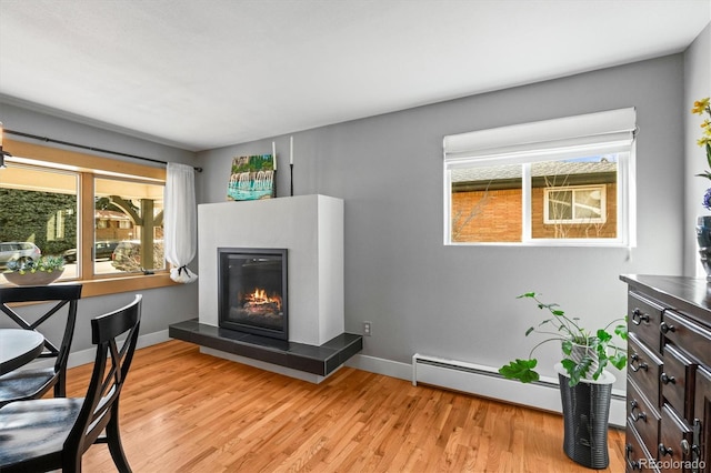 living area with a glass covered fireplace, light wood-style flooring, a baseboard heating unit, and baseboards