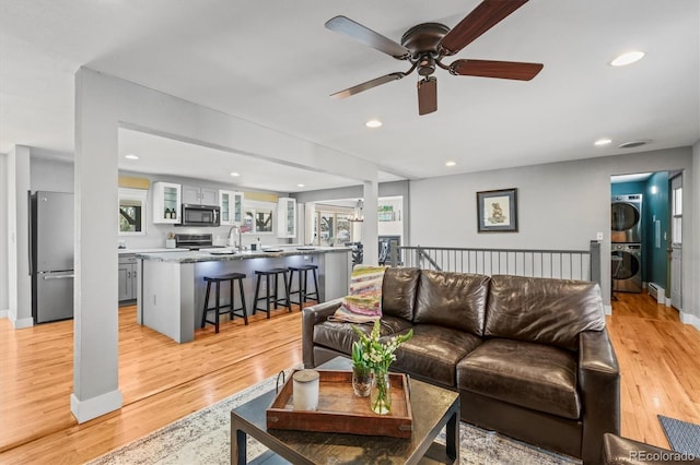 living room featuring light wood-style flooring, a ceiling fan, recessed lighting, stacked washer / dryer, and baseboards