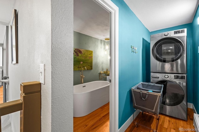 laundry area with laundry area, wood finished floors, baseboards, and stacked washer and dryer