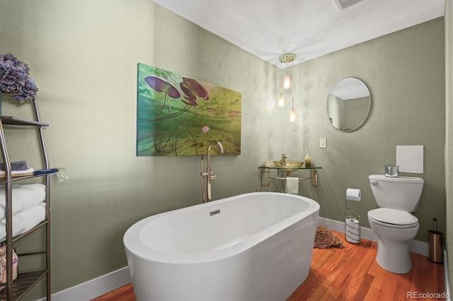 bathroom with toilet, wood finished floors, baseboards, and a freestanding bath